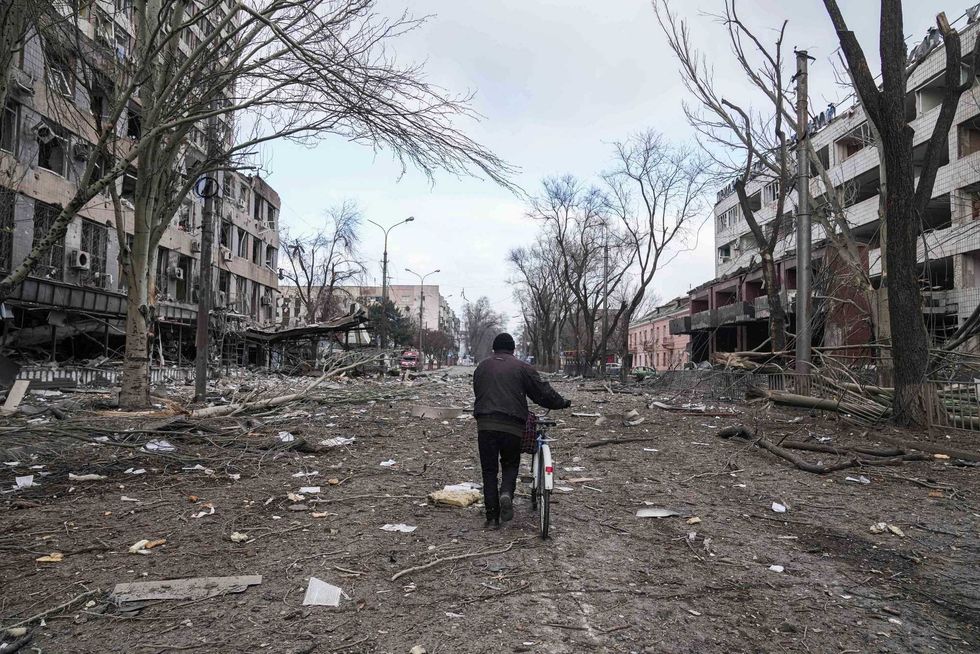 A man walks with a bicycle in a street damaged by shelling in Mariupol, Ukraine, Thursday, March 10, 2022