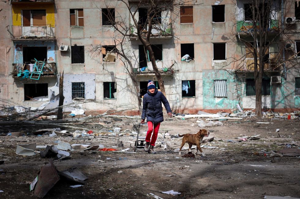 A man walks with his dog near an apartment building damaged by shelling from fighting on the outskirts of Mariupol, Ukraine, in the territory controlled by the breakaway Donetsk People