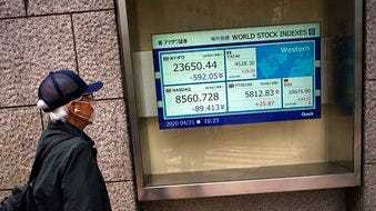 A man wearing a mask against the spread of the new coronavirus looks at an electronic stock board showing world stock indexes at a securities firm in Tokyo Tuesday, April 21, 2020. (AP Photo/Eugene Hoshiko)