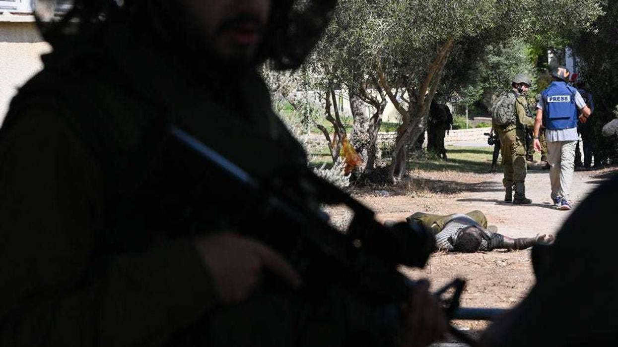 A member of the media and IDF soldiers walk past a Hamas militant who was killed days earlier after attacking this kibbutz where dozens of civilians were killed near the border with Gaza, on October 10, 2023 in Kfar Aza, Israel. Israel has sealed off Gaza and conducted airstrikes on Palestinian territory after an attack by Hamas killed hundreds and took more than 100 hostages. On October 7, the Palestinian militant group Hamas launched a surprise attack on Israel from Gaza by land, sea, and air, killing over 700 people and wounding more than 2000. Israeli soldiers and civilians have also been taken hostage by Hamas and moved into Gaza. The attack prompted a declaration of war by Israeli Prime Minister Benjamin Netanyahu, and ongoing retaliatory strikes by Israel on Gaza killing hundreds.(Photo by Alexi J. Rosenfeld/Getty Images)