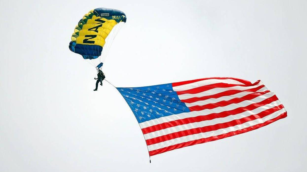 A member of the U.S. Navy Parachute Team "The Leap Frogs" parachutes with an American flag at Wrigley Field before the game between the Chicago Cubs and the Milwaukee Brewers on August 15, 2018 in Chicago, Illinois