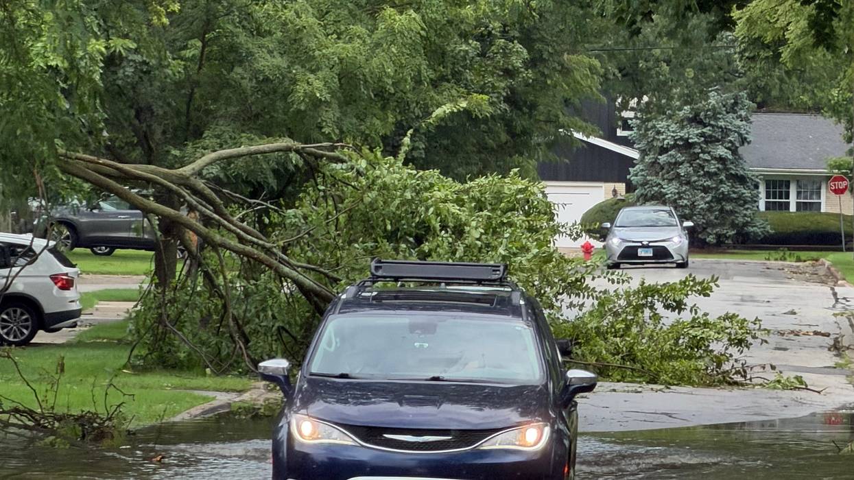 A minivan drives through a flooded street in Homewood, Illinois, as part of a tree lays in the road behind it.