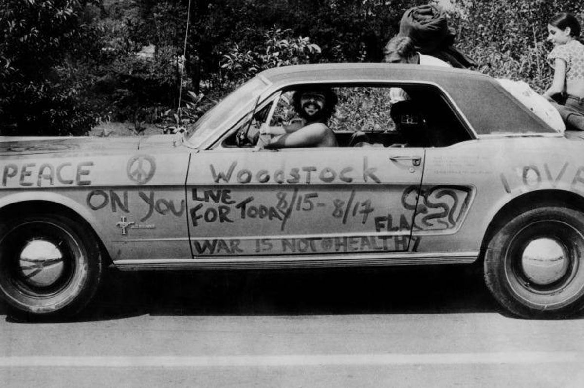 A music fan at Woodstock pop festival in his car covered in anti-war slogans for love and peace.