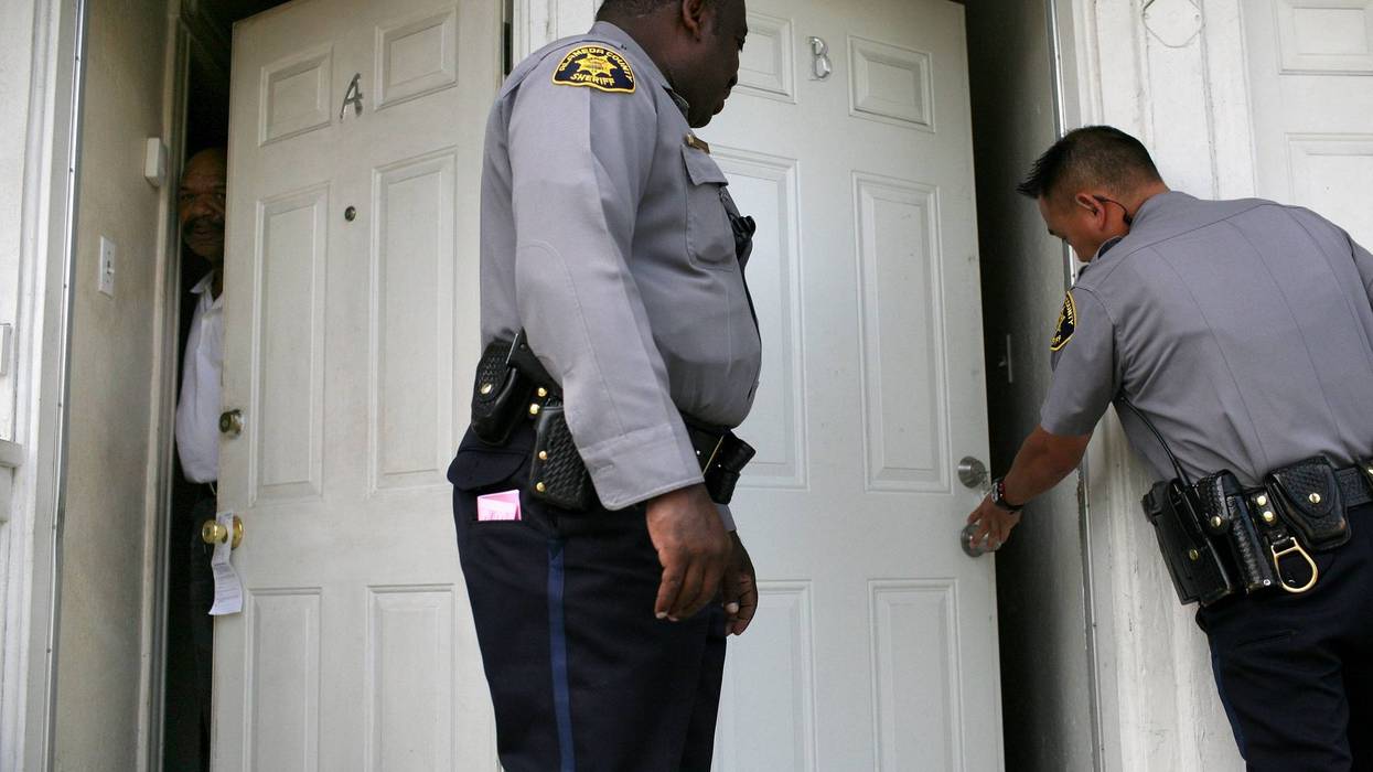 A neighbor peers out of his door as Alameda County Sheriff deputies Ken Cammack (C) and Ken Kong (R) enter an apartment to evict tenants who have defaulted on rent payments June 4, 2009.