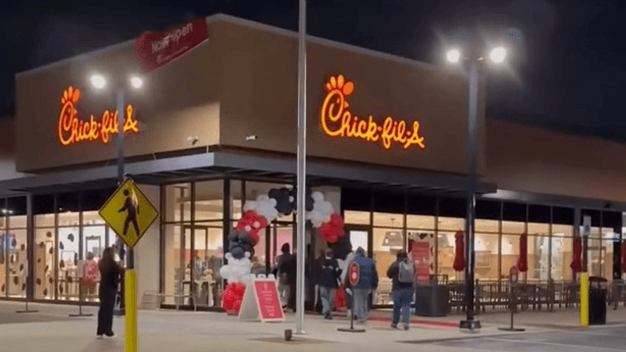 A new Chick-fil-A restaurant brightly lit at night, with people entering under a festive balloon arch.