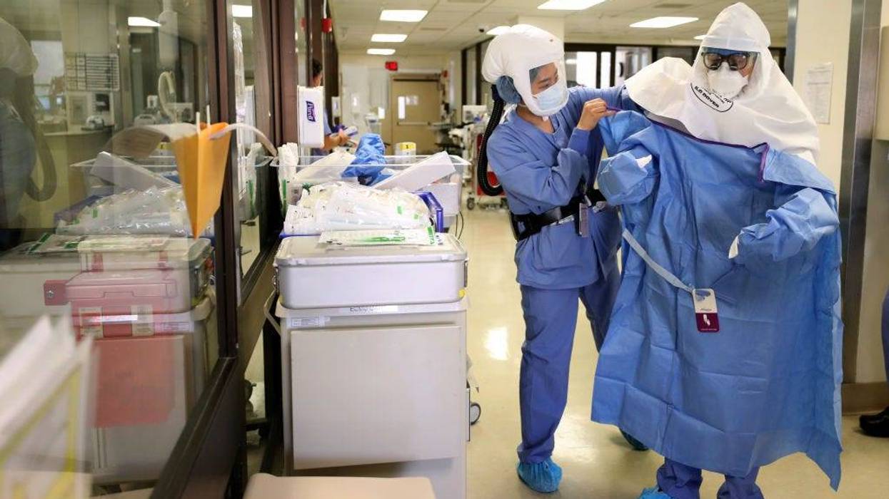 A nurse helps a doctor put on his personal protective equipment (PPE)