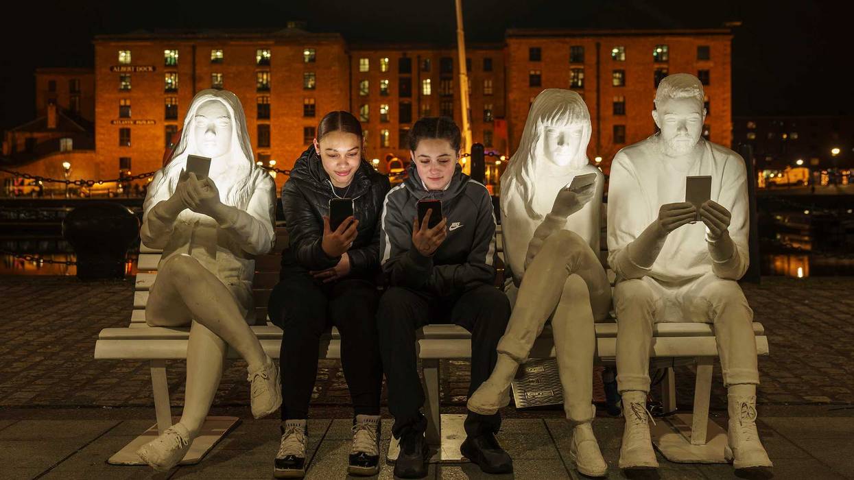 A pair of teens sit with their smartphones in Liverpool, England.