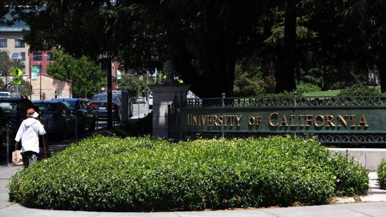 A pedestrian walks by a sign in front of the U.C. Berkeley campus.