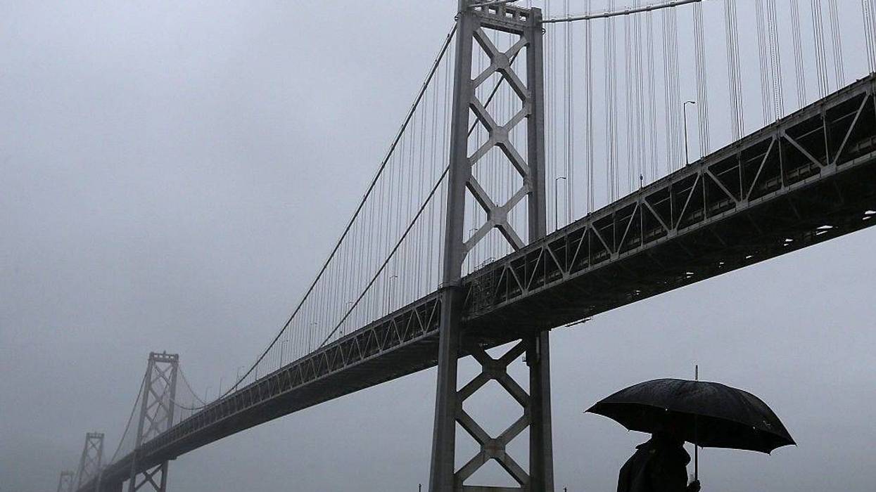 A pedestrian walks in the rain next to the San Francisco-Oakland Bay Bridge on December 11, 2014 in San Francisco, California.