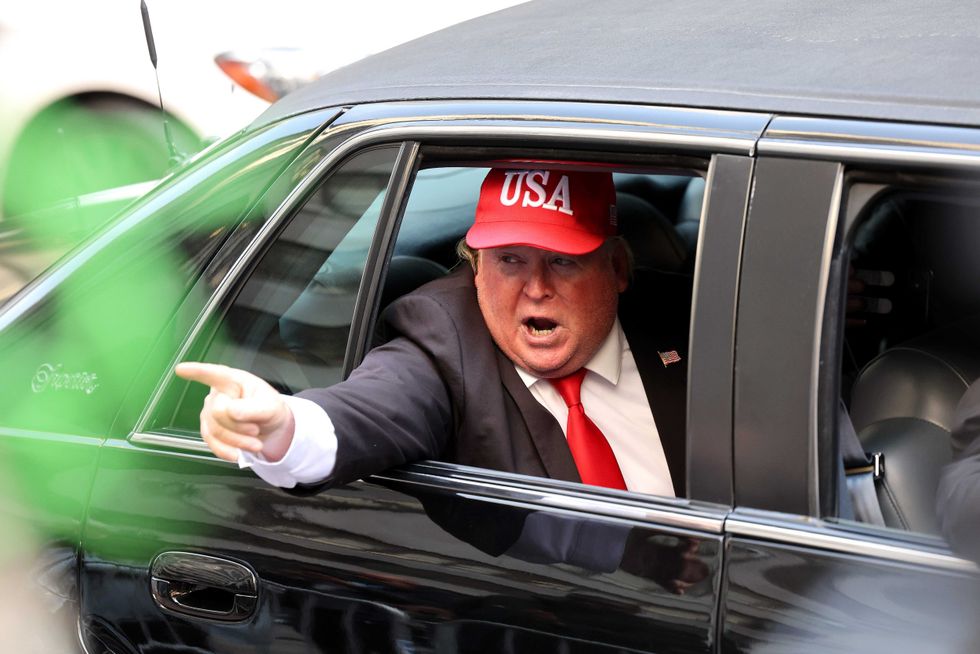 A person dressed as former President Donald Trump rides in a car past Trump Tower on April 04, 2023