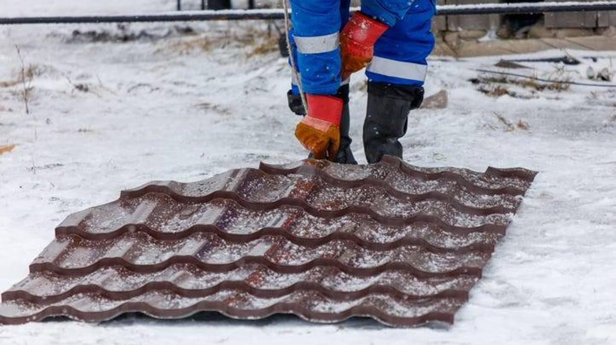 A person in a blue suit is walking on a snow covered roof. The person is wearing orange gloves and boots