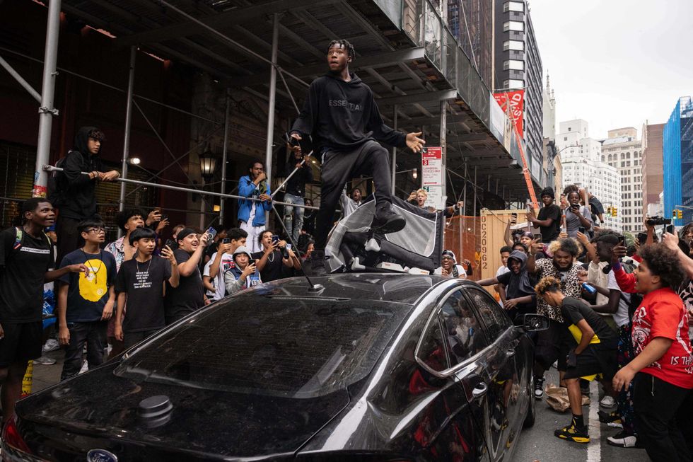 A person jumps on an NYPD vehicle during a riot in the Union Square area on Aug. 4, 2023