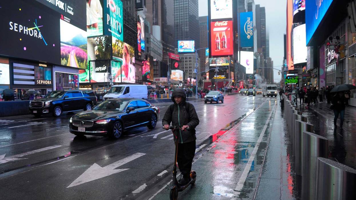 A person rides an electric scooter through Times Square, New York City on a rainy day