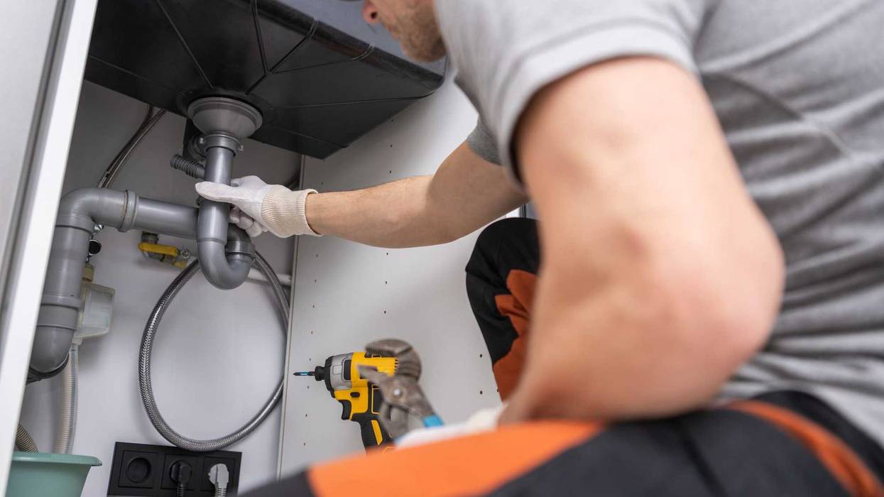 A plumber works on a drain pipe.