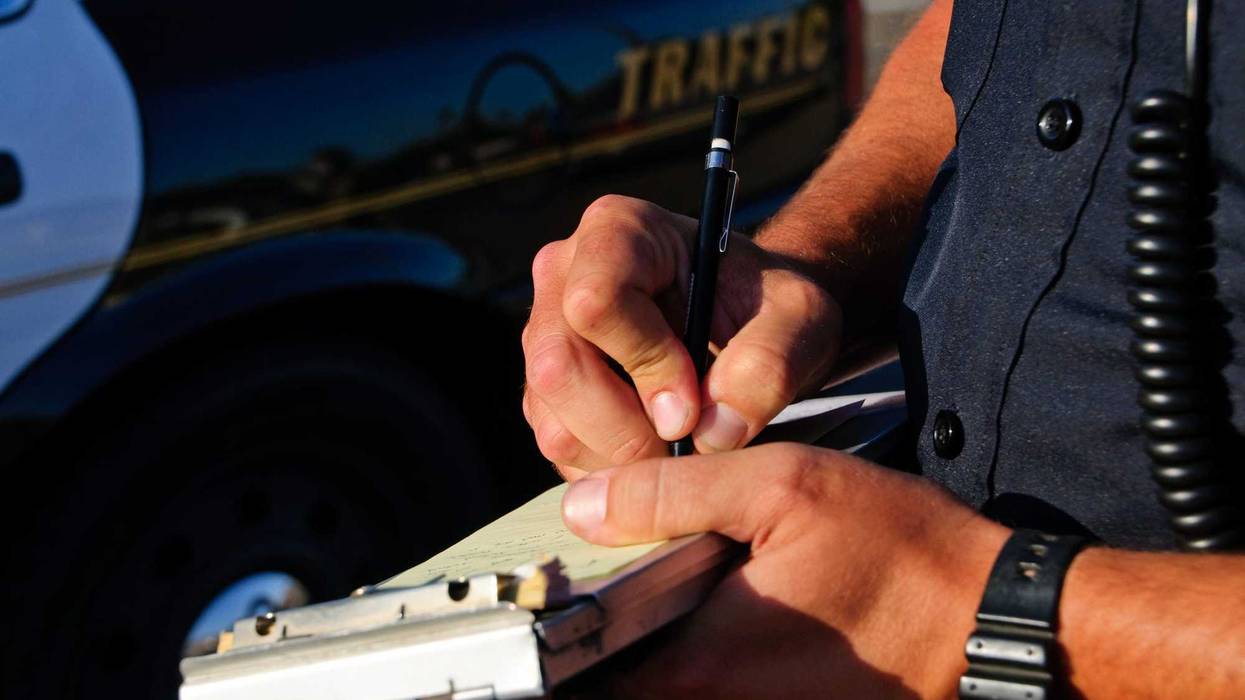 A police officer on the side of the road as he writes a ticket.