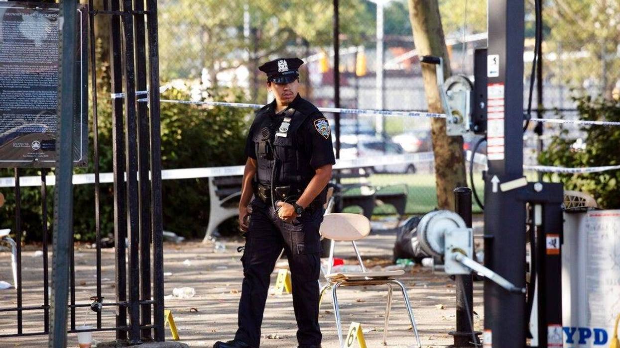 A police officer walks by yellow evidence markers at a playground in the Brownsville neighborhood in the Brooklyn borough of New York, Sunday, July 28, 2019. Police said, one man was killed and at least 11 others were injured in a shooting late Saturday n