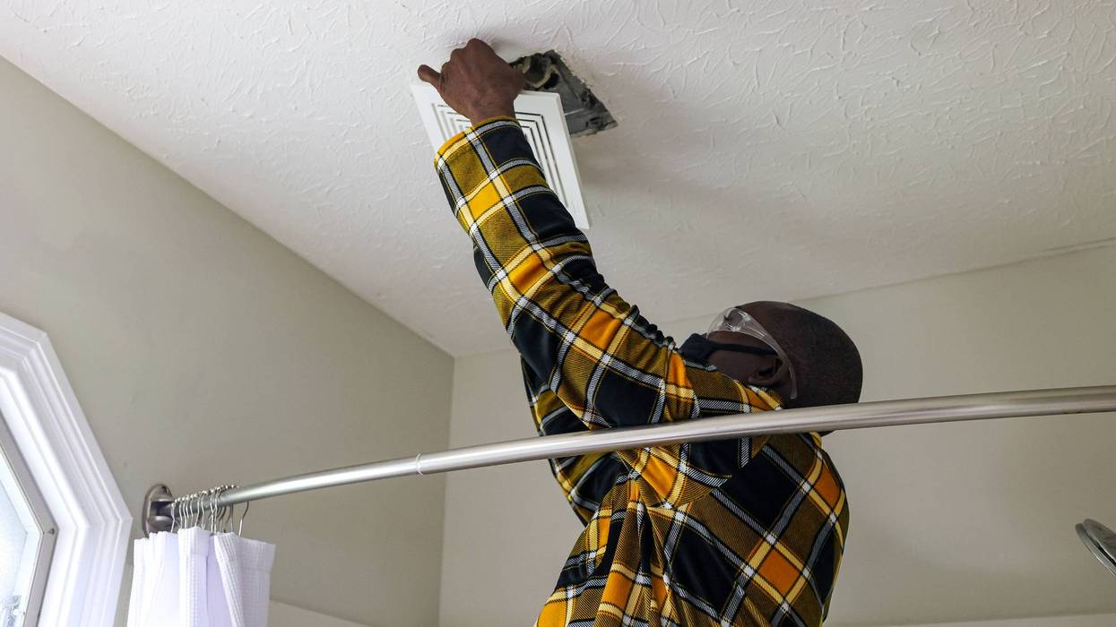 A portrait of a black man cleaning a bathroom vent