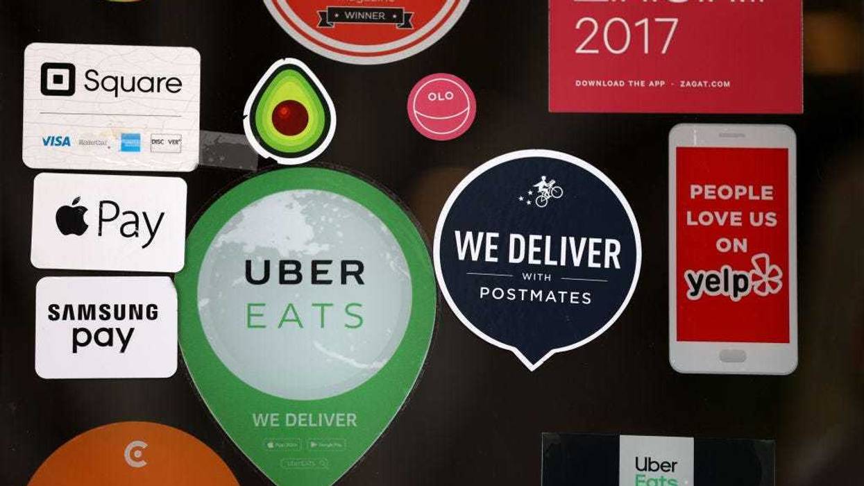A Postmates sticker is displayed next to an Uber Eats sticker on the window of a restaurant on July 06, 2020 in San Francisco, California.