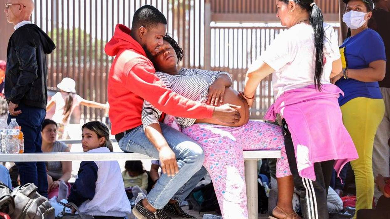 A pregnant immigrant from Haiti is assisted by her partner and another immigrant while having contractions, after she crossed from Mexico, with the U.S.-Mexico border barrier in the background, on May 21, 2022 in San Luis, Arizona. A U.S. Border Patrol agent soon opened a gate in the border barrier to allow paramedics to reach her, while was still technically in the United States. She had been stranded behind the barrier with other immigrants, some of whom said they had been waiting for two days to be picked up by Border Patrol. Title 42, the controversial pandemic-era border policy enacted by former President Trump, which cites COVID-19 as the reason to rapidly expel asylum seekers at the U.S. border, was set to officially expire on May 23rd. A federal judge in Louisiana delivered a ruling yesterday blocking the Biden administration from lifting Title 42. (Photo by Mario Tama/Getty Images)