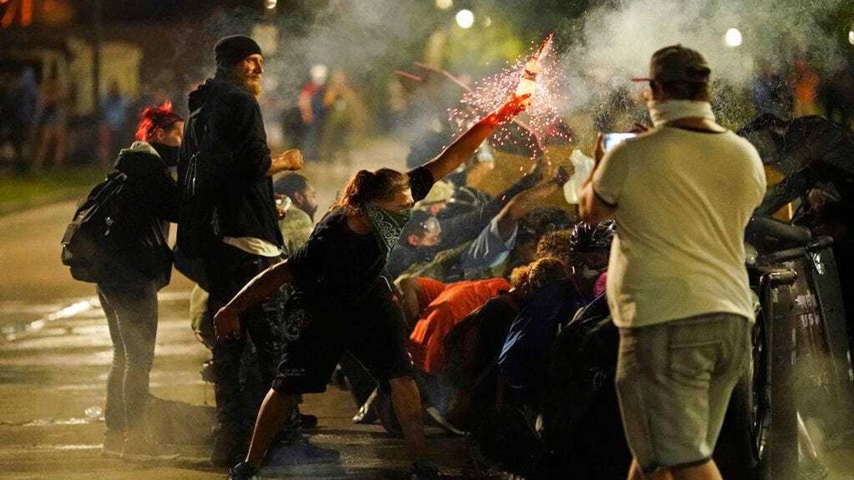 A protester tosses an object toward police during clashes outside the Kenosha County Courthouse late Tuesday, Aug. 25, 2020, in Kenosha, Wis., on third night of unrest following the shooting of a Black man, Jacob Blake.