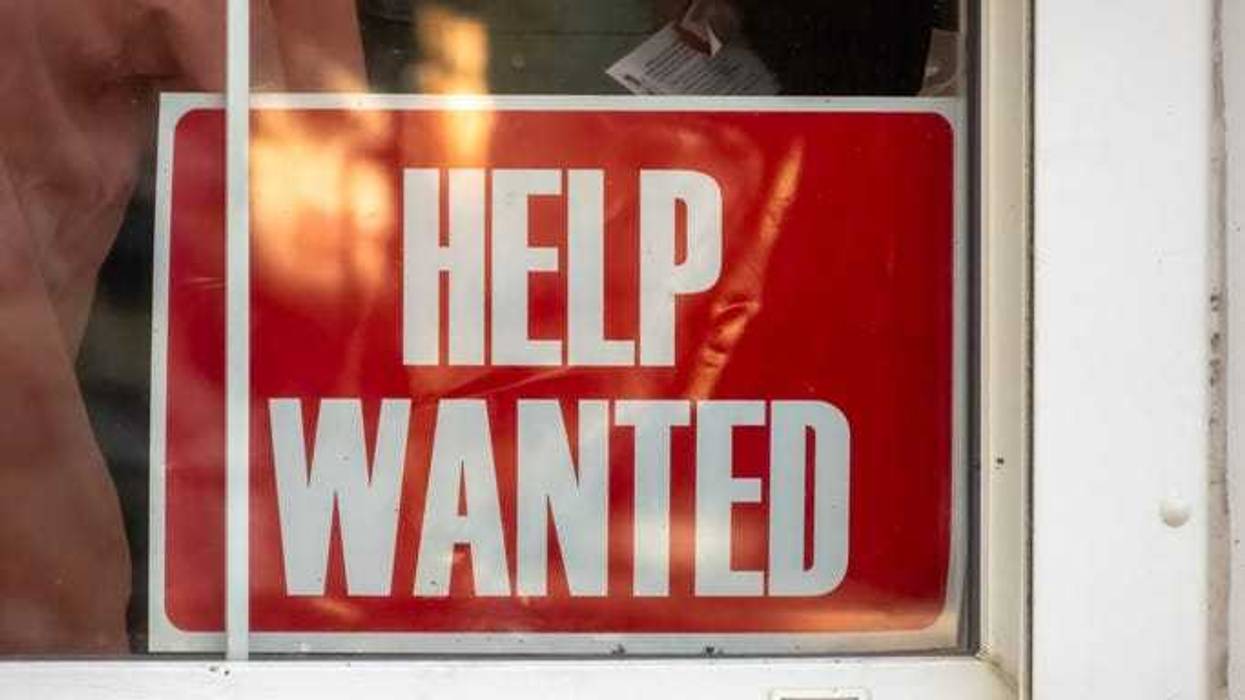 A red HELP WANTED sign displayed prominently in a store window, signaling the business's need for additional staff.