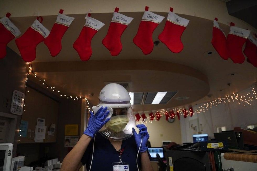 A registered nurse disinfects her powered air purifying respirator in a COVID-19 unit decorated with Christmas stockings.