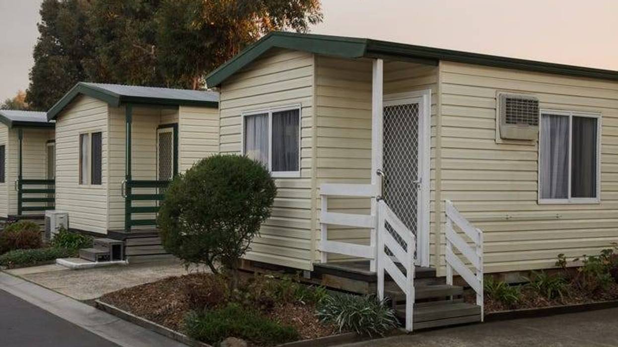 A row of mobile homes including one with a white fence up the porch stairs a bush out front.