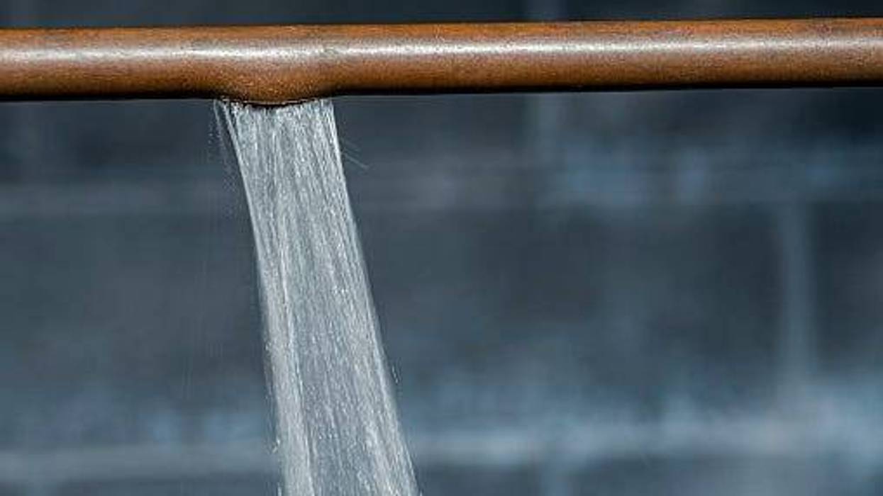 A ruptured copper pipe spraying water against a basement wall