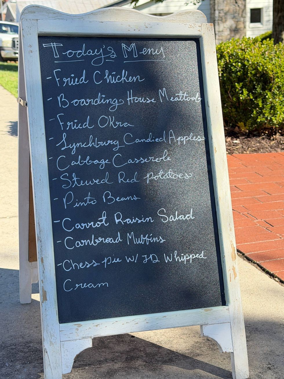 A rustic chalkboard menu on a sidewalk lists Southern dishes like fried chicken and chess pie. The setting feels cozy and inviting.