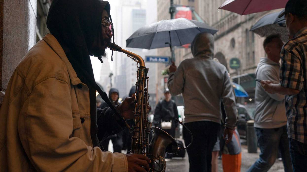 A saxophonist plays in Manhattan as people walk by on Saturday. The weekend's rainy weather continues this week