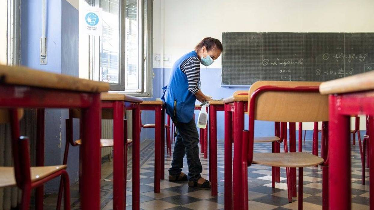 A school worker disinfects the desks at the end of the first day of school on September 15, 2020 in Turin, Italy.