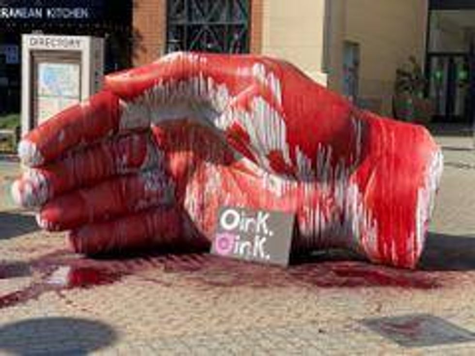 A sculpture is covered in blood, a sign reading "oink oink."