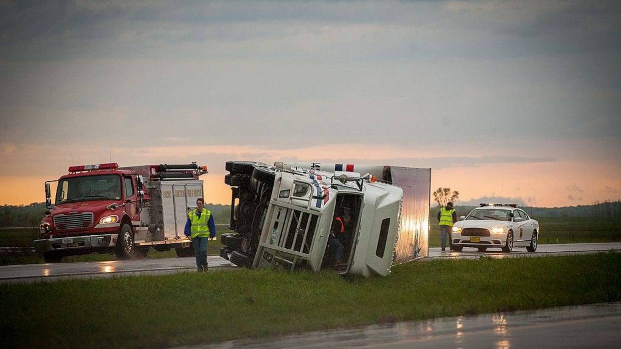 A semi-trailer truck on its side on the road, plus a fire truck.