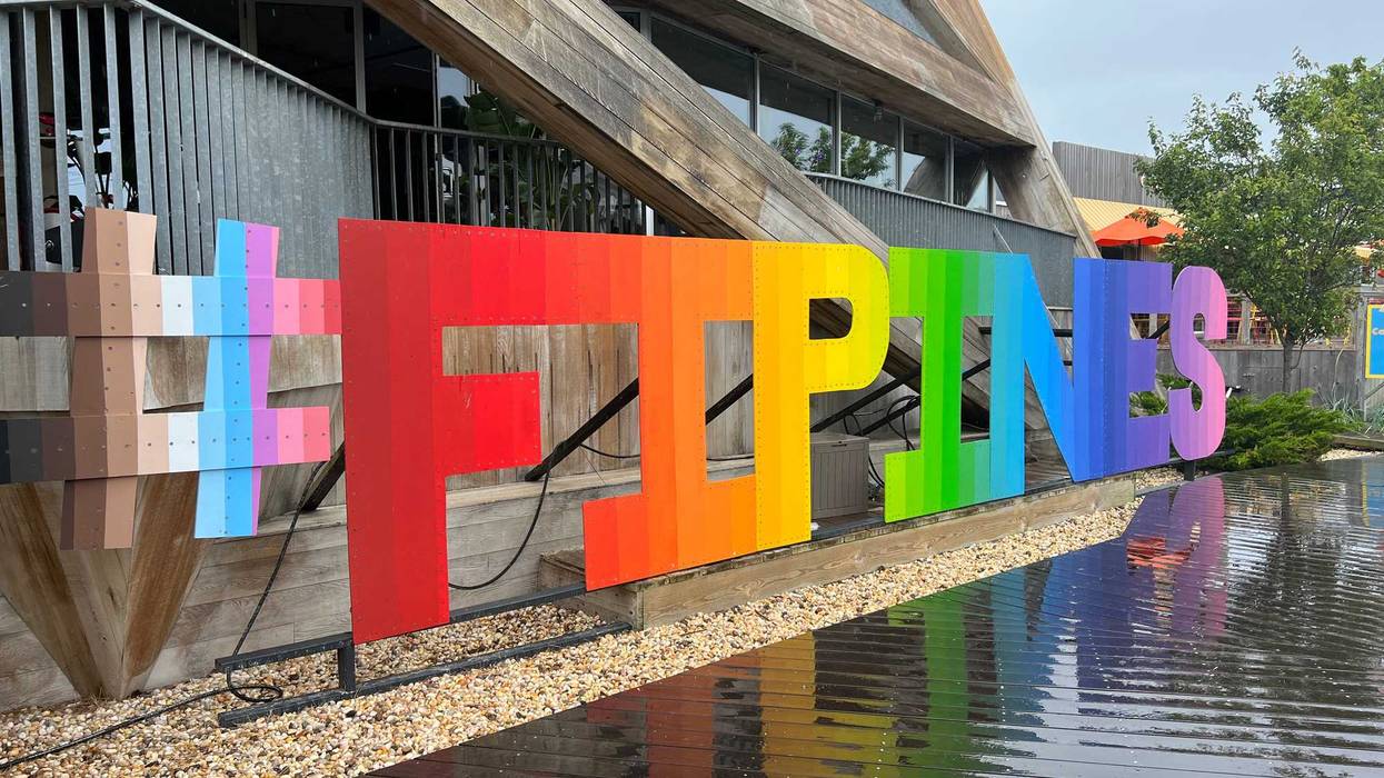 A sign for the Fire Island Pines decked out in the colors of the rainbow greets you at the ferry dock