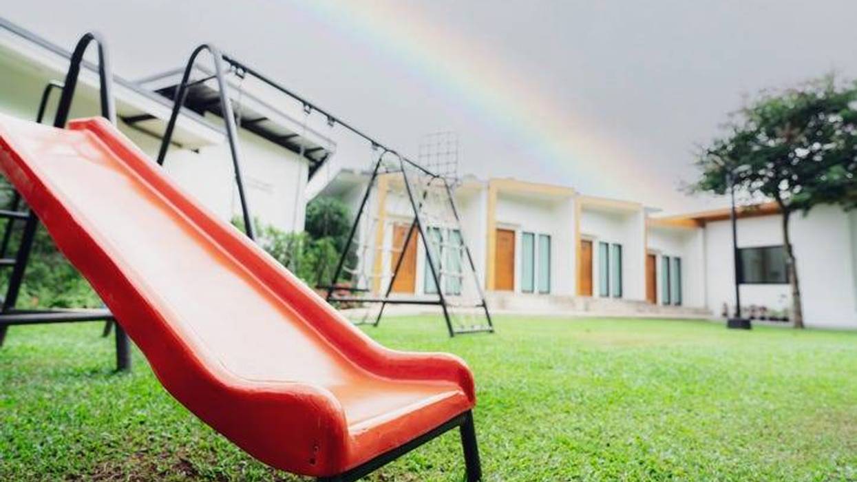 A slide and swing set sitting empty in front of a child care center with a rainbow in the back