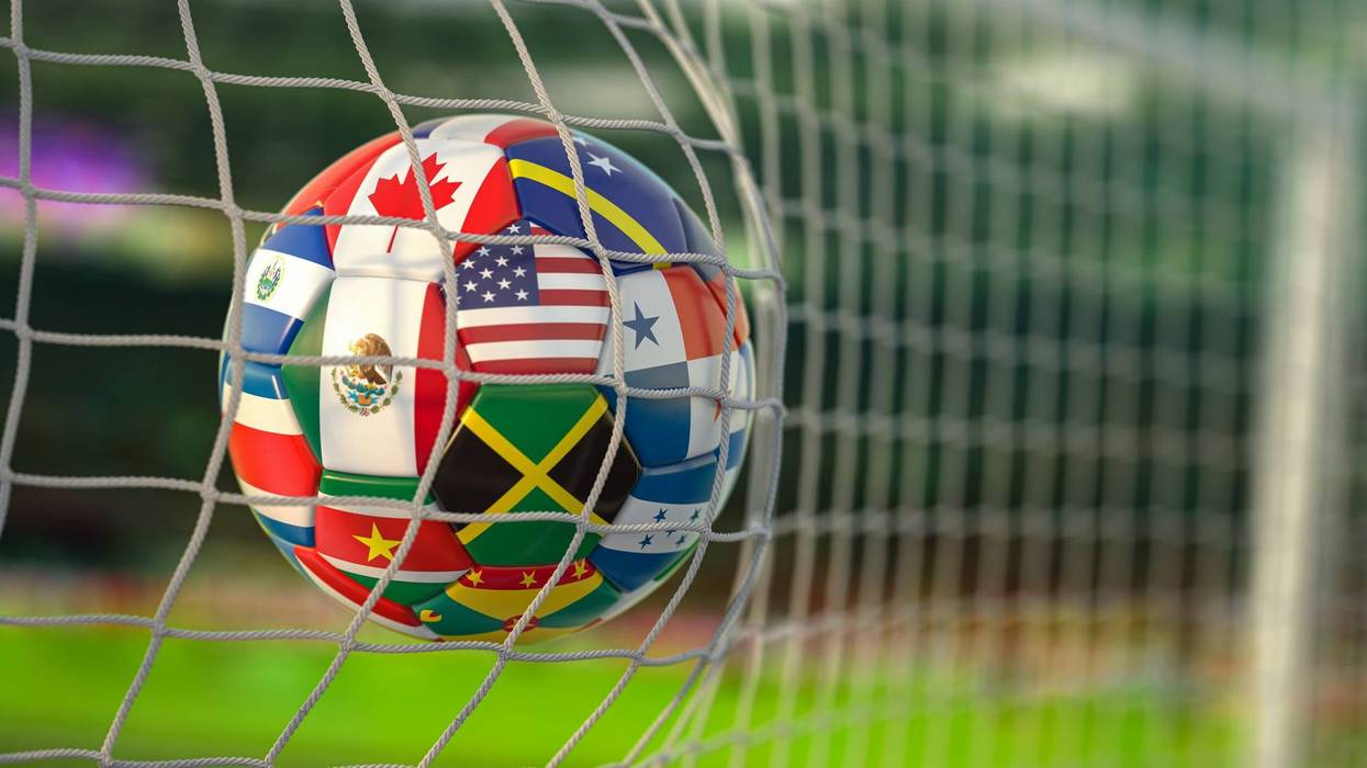 A soccer ball covered in world flags goes into the net of a soccer goal