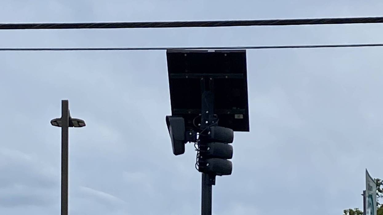 A solar-powered Flock camera on a pole under an overcast sky with power lines overhead.