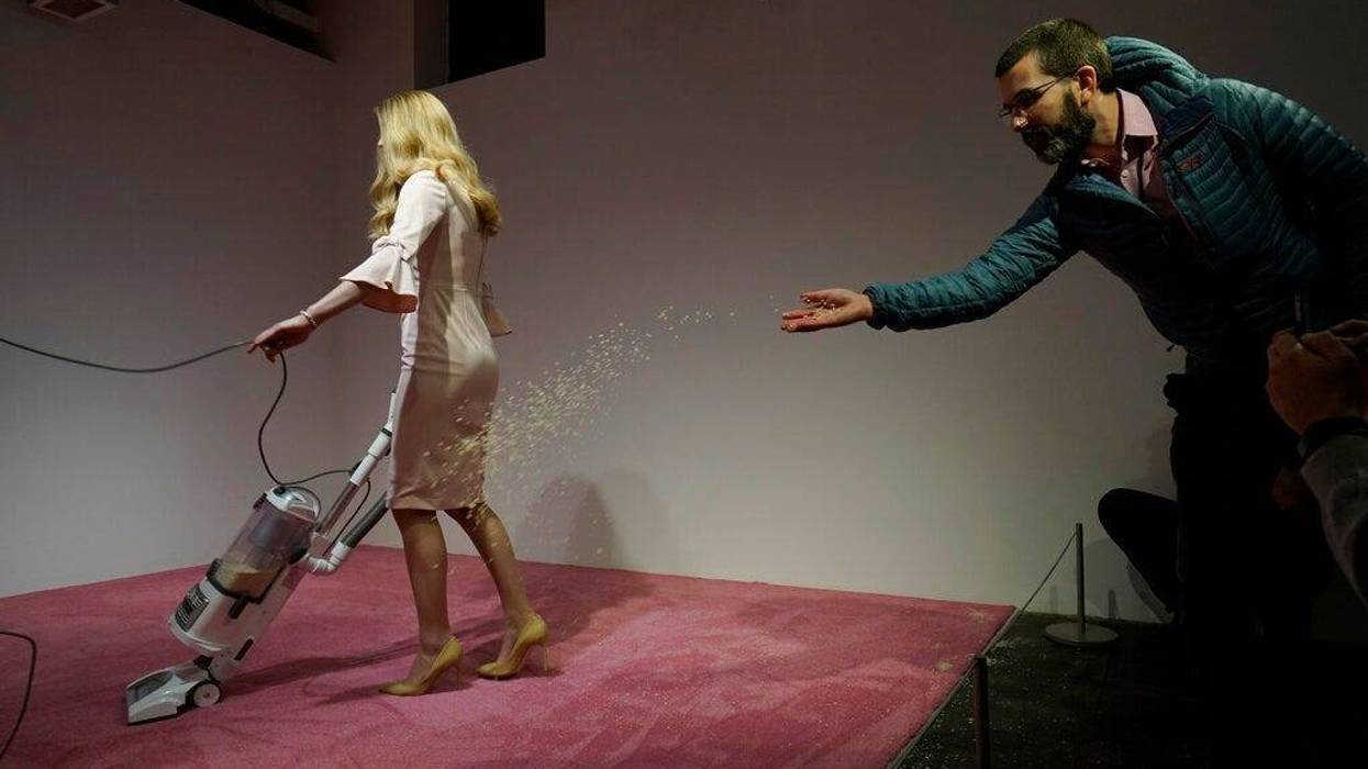 A spectator tosses crumbs for an Ivanka Trump lookalike to vacuum at Jennifer Rubell's art exhibit "Ivanka Vacuuming 2019" on Tuesday, Feb. 5, 2019