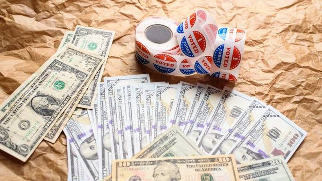 A stack of hundred dollar bills is fanned out on a table next to a roll of stickers that read "I voted."