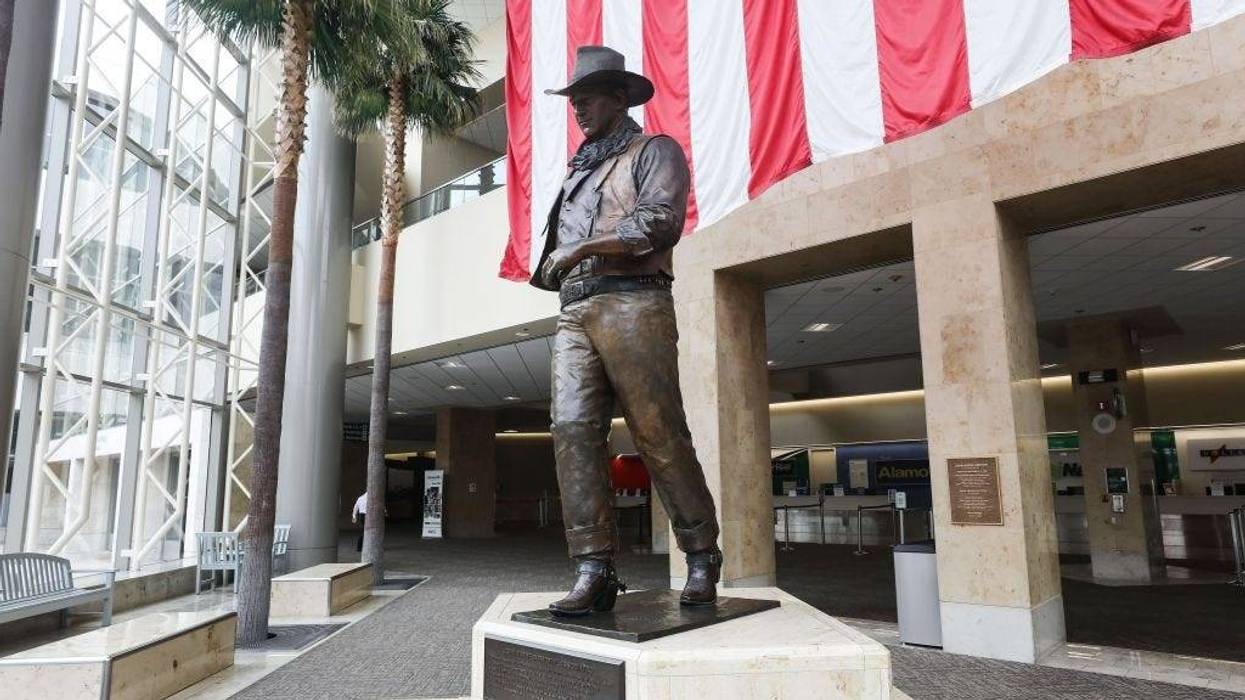A statue of John Wayne is on display beneath an American flag in John Wayne Airport, located in Orange County, on June 28, 2020 in Santa Ana, California.