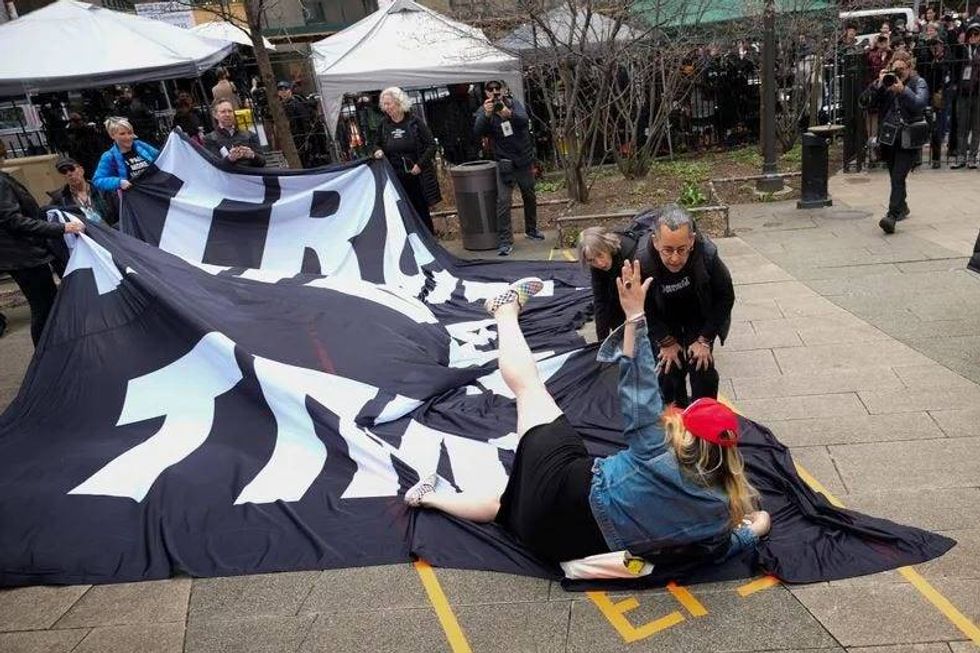 A supporter of Donald Trump tumbles to the ground on top of a banner criticizing him outside the courthouse where Trump will arrive later in the day for his arraignment on April 4, 2023.