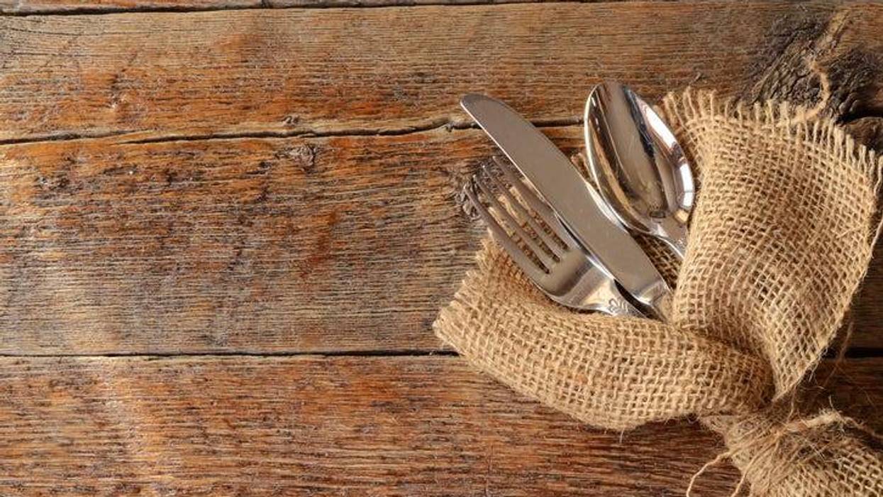 A top view image of eating utensils wrapped in burlap on a wooden table.
