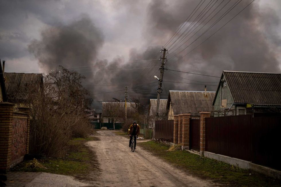 A Ukrainian man rides his bicycle near a factory and a store burning after it had been bombarded in Irpin, on the outskirts of Kyiv, Ukraine, Sunday, March 6, 2022