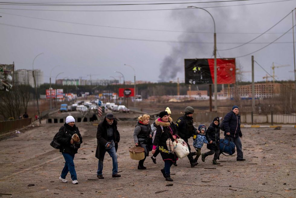 A Ukrainian police officer helps people as artillery echoes nearby while fleeing Irpin in the outskirts of Kyiv, Ukraine, Monday, March 7, 2022