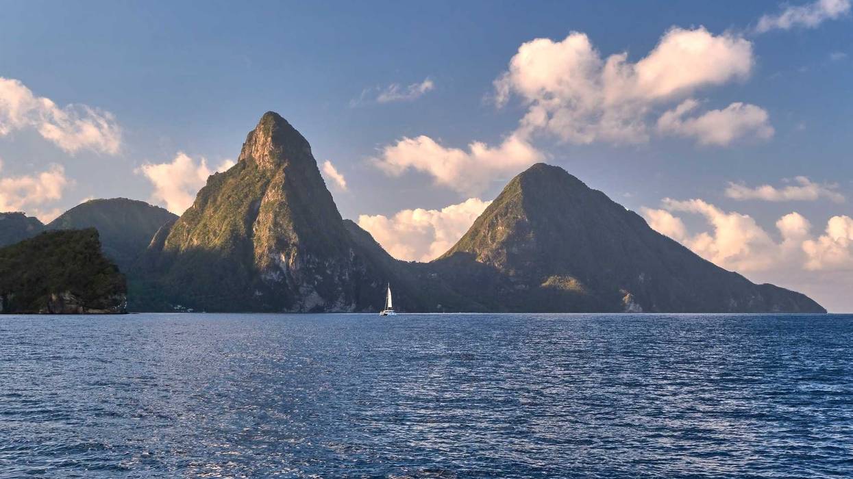 A UNESCO heritage site, the two Pitons of St Lucia, dwarfing a sailboat, are seen from the water at sunrise.