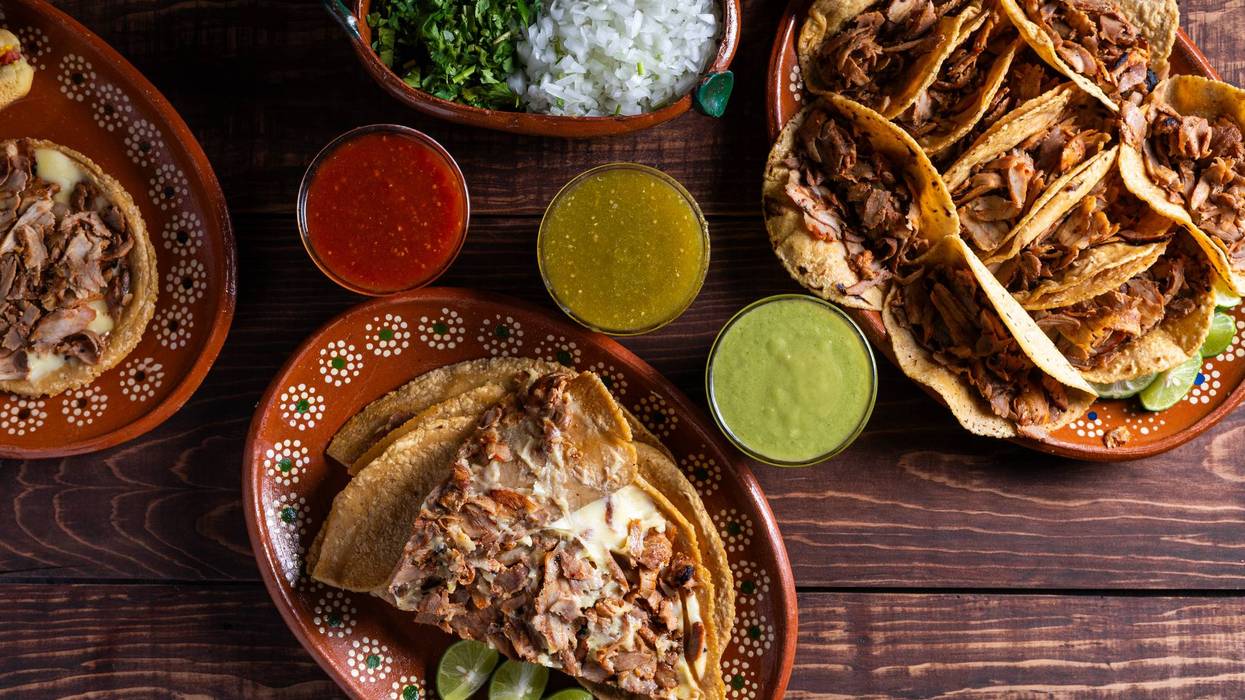 A variety of Mexican street tacos served with salsa and garnishes on a rustic wooden table.