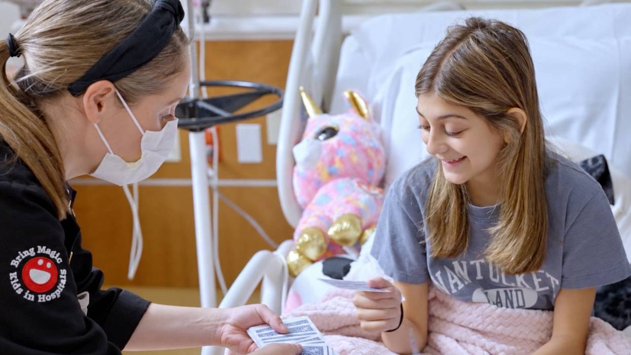 A volunteer with Bring Magic to Kids in Hospitals (formerly Open Heart Magic) performs a magic trick for a young patient.