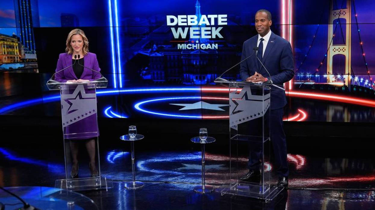 A woman and man on a debate stage for 'Debate Week Michigan,' with glowing blue and red lights.