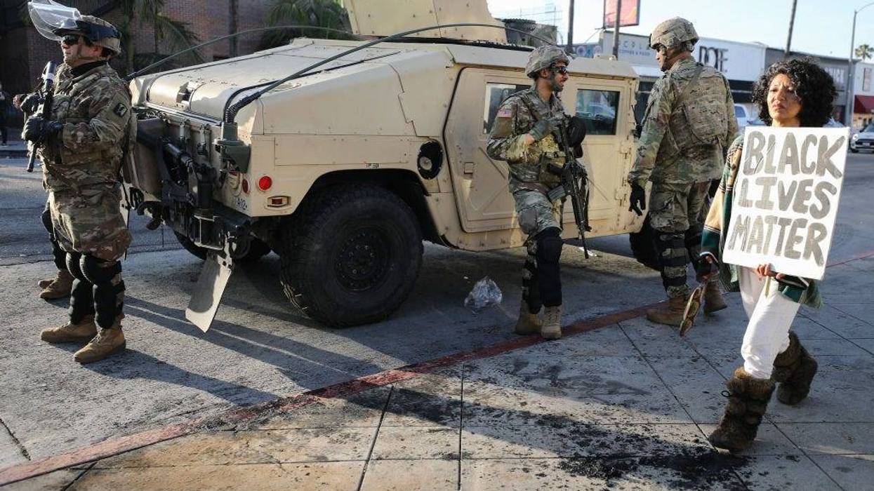 A woman carries a 'Black Lives Matter' sign past U.S. National Guard troops in the Fairfax District, an area damaged during yesterday's unrest, after the troops were activated by California Governor Gavin Newsom following violent demonstrations.