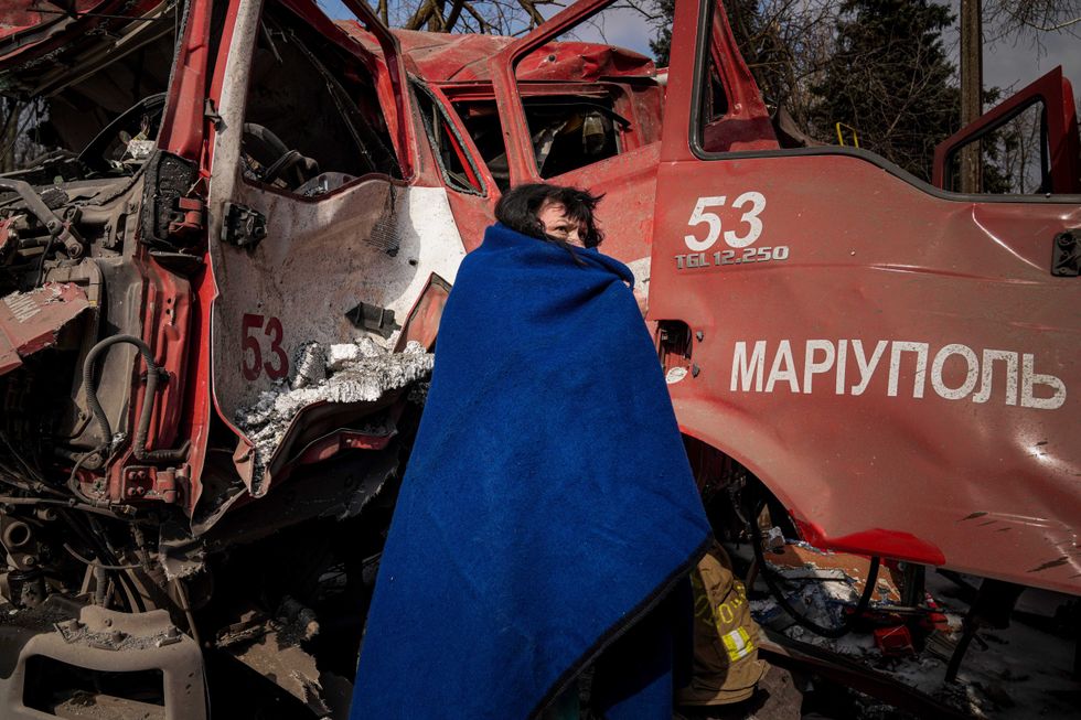A woman covers herself with a blanket near a damaged fire truck after shelling in Mariupol, Ukraine, Thursday, March 10, 2022